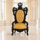 An ornate royal-style throne chair with a carved black wooden frame and a tufted mustard yellow leather seat and backrest, set in a grand, sunlit palace hall with marble floors and windows.