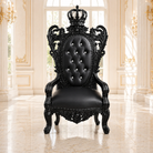 A black ornate throne-style armchair with carved details, a tufted backrest, and a crown topper, shown in a bright classical interior with cream walls and marble floors.
