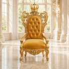 An ornate gold throne chair with a tufted mustard yellow backrest and seat, featuring a crown on the backrest, set in a bright, classical hall with white columns and marble floors.