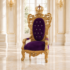 An ornate royal-style armchair with a gold carved frame, purple velvet upholstery, and a crown on the backrest, set in a bright classical interior with white columns and windows.