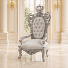 A royal-style baroque armchair with an ornate silver carved frame, a tufted cream backrest, and a crown on top, set in an elegant cream-colored palace interior with marble floors.