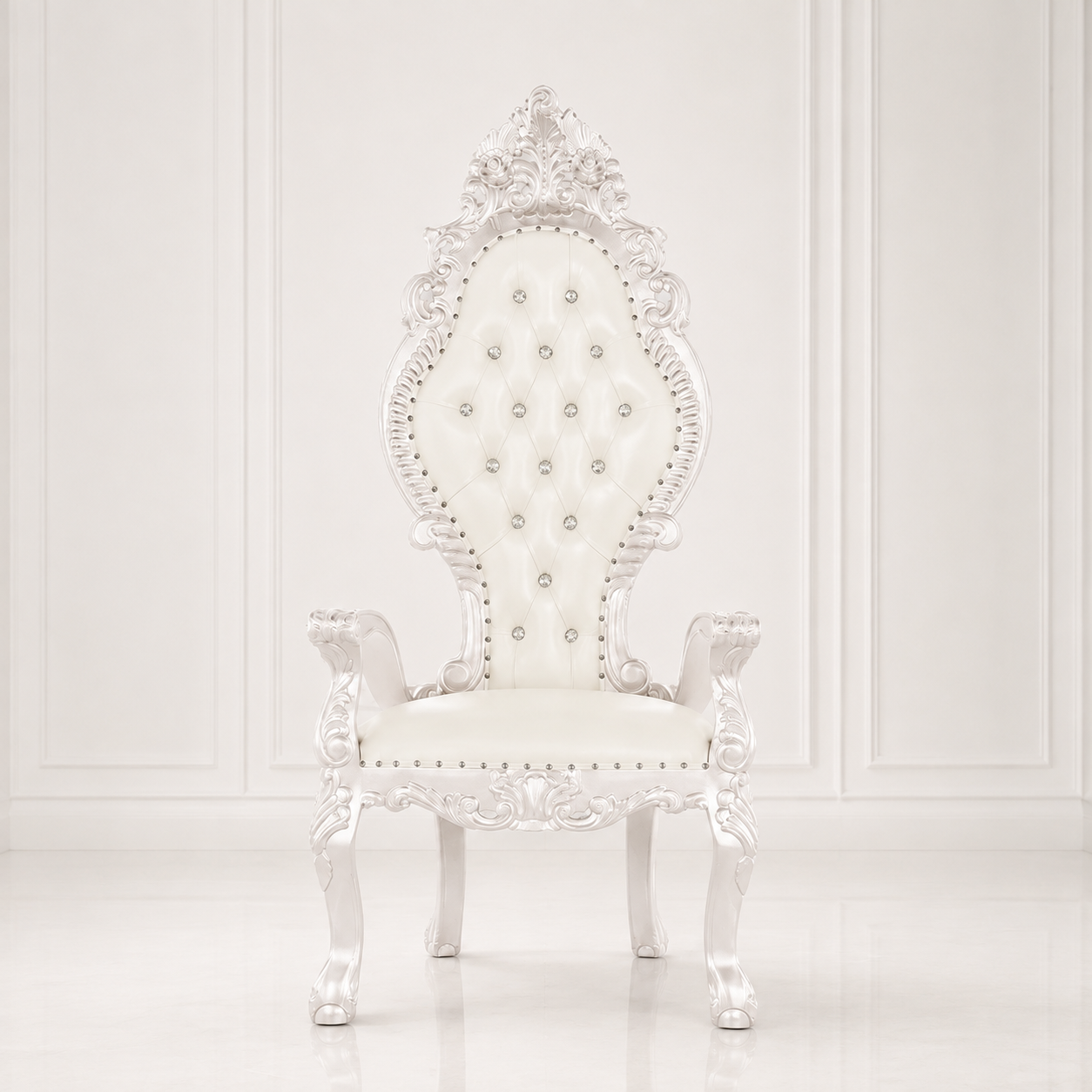 A white baroque-style high-back vanity chair with tufted upholstery, ornate carved details, and silver nailhead accents, set against a white paneled wall background.