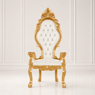 An ornate high-back throne chair with a carved gold frame and white tufted upholstery, set against a white paneled wall and floor.